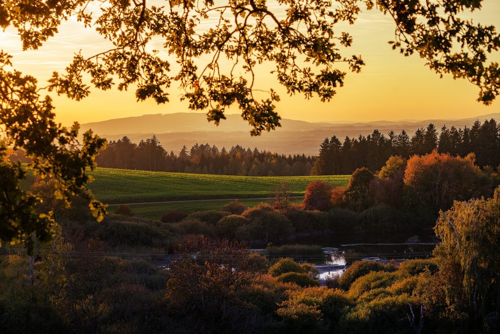 Eine hügelige Landschaft, die durch den Sonnenunter in den Farben Geld, Orange und Rot erscheint.