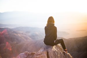 Frau sitzt auf einem Felsen und schau auf die Sonne