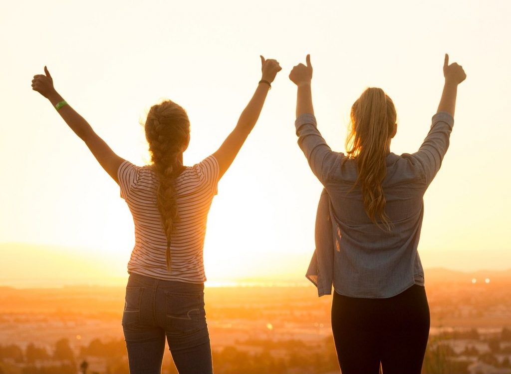 Zwei Frauen im Sonnenuntergang – ©StockSnap/Pixabay Zwei Frauen stehen mit hochgereckten Daumen auf einem Aussichtspunkt und schauen in den Sonnenuntergang.