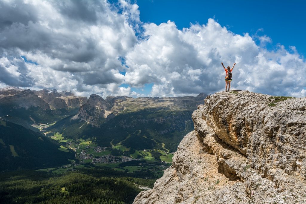Wanderin am Ziel - ©Free-Photos/Pixabay Eine Wanderin steht auf einem Felsen, streckt die Arme nach oben und schaut in das Tal vor ihr.