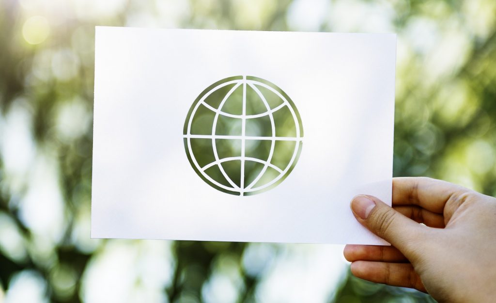 Weltkugel auf Papier – ©/Pixabay Ein Papier mit ausgeschnittener Weltkugel wird vor einem verschwommenen Hintergrund mit Bäumen gehalten.